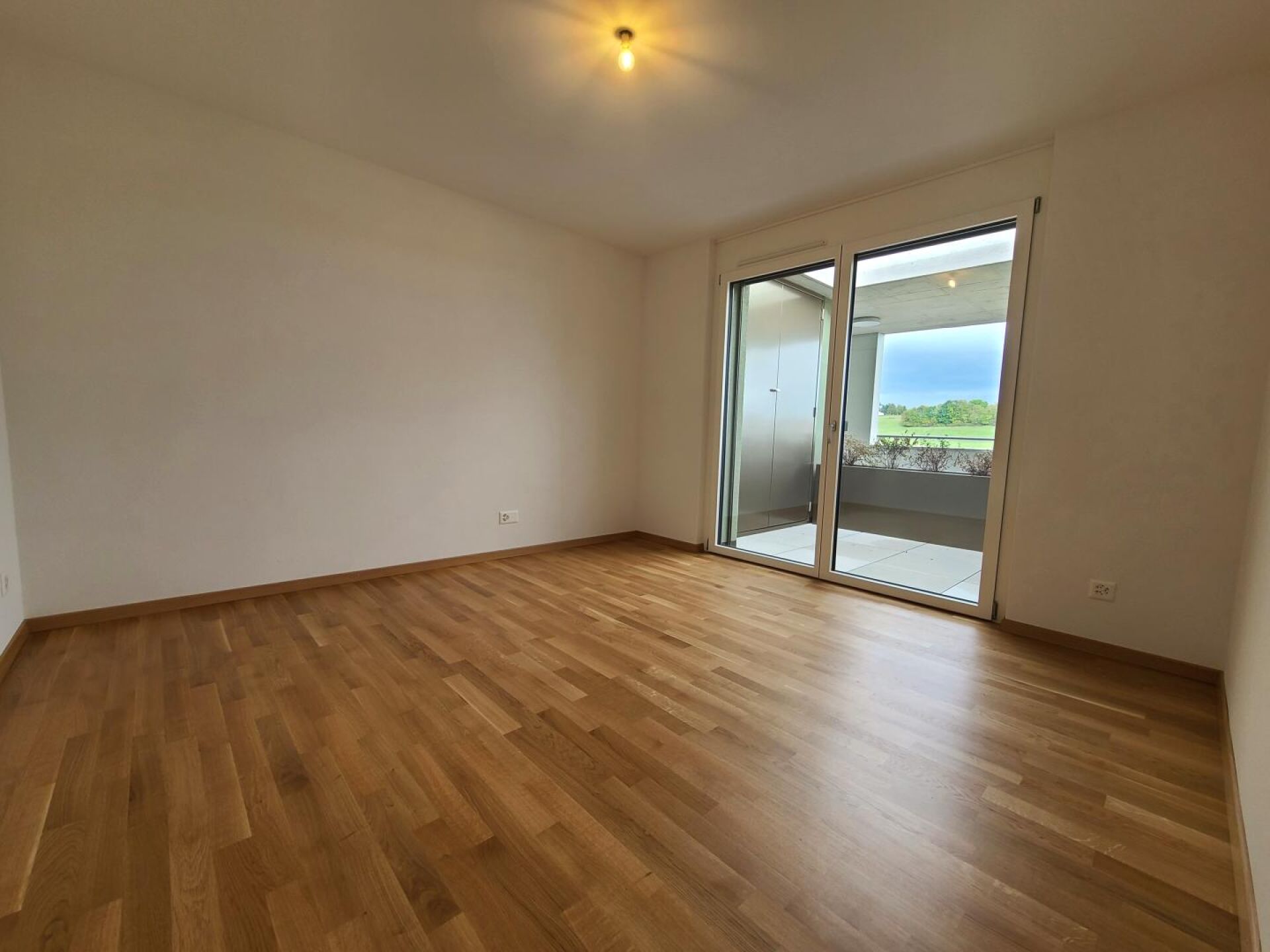 Leerer, heller Raum mit Parkettboden und Balkonblick