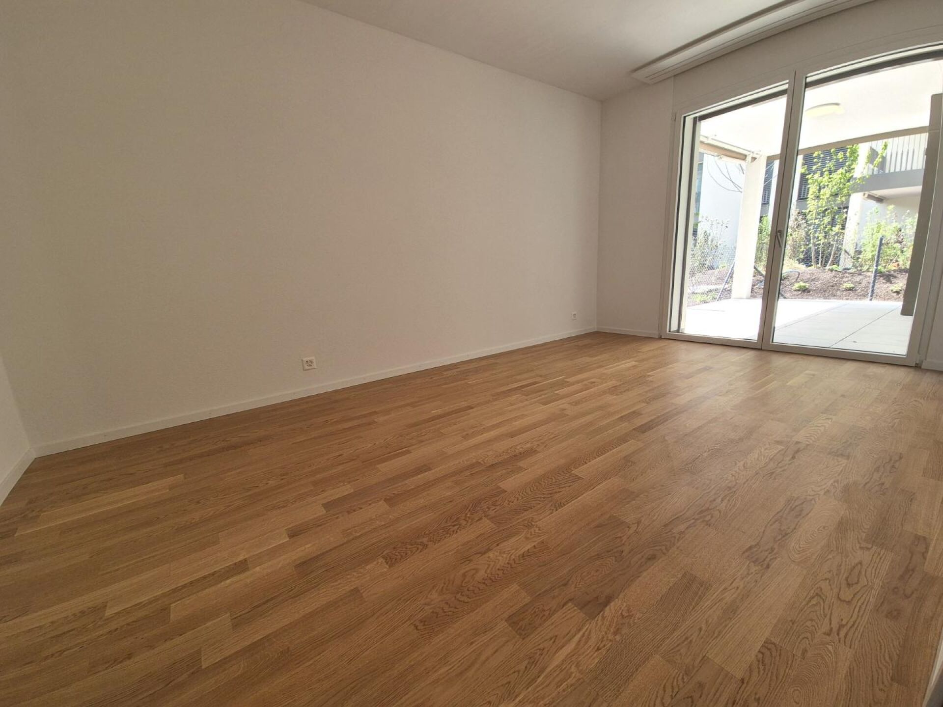 Leerer Wohnraum mit Holzboden und Terrassentür