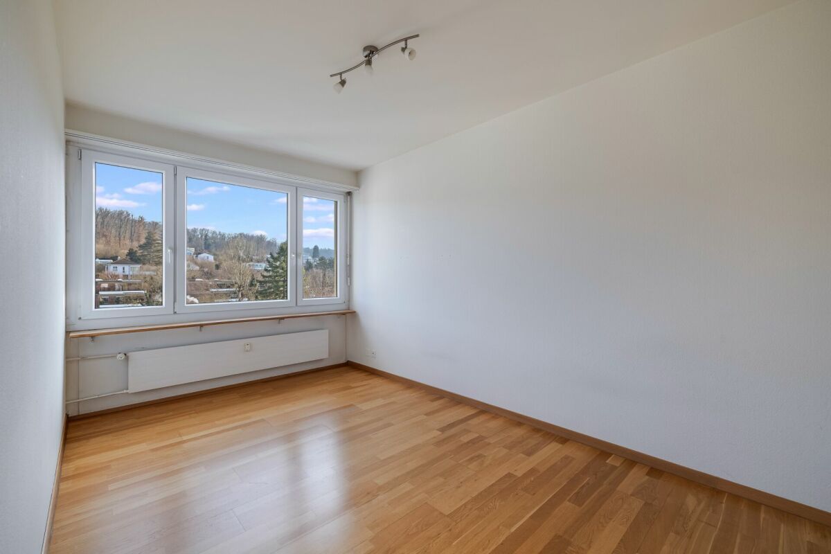 Helles, leeres Zimmer mit großem Fenster und Parkettboden