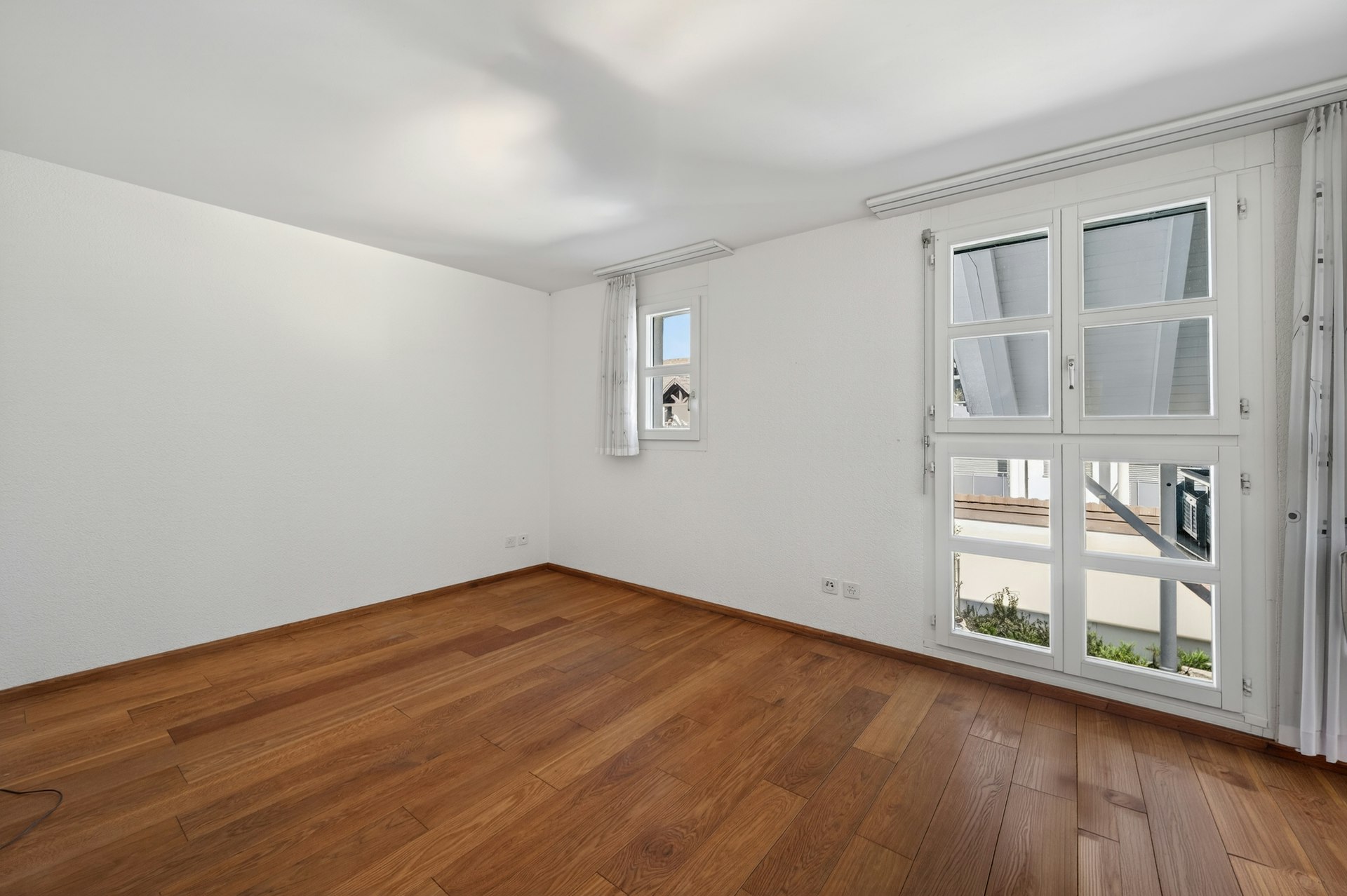 Heller leerer Wohnraum mit Holzfußboden und großen Fenstern
