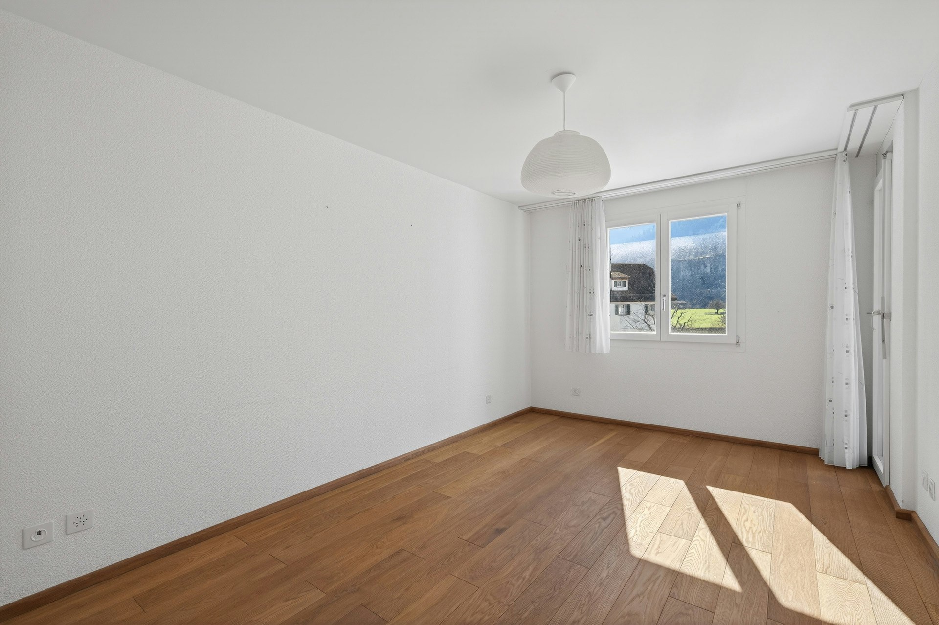 Helles, leeres Zimmer mit Holzfußboden und Fensterblick