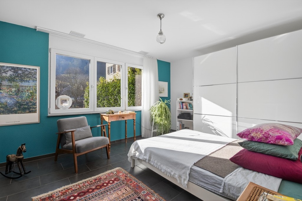 Helles Schlafzimmer mit türkisfarbener Akzentwand und großen Fenstern