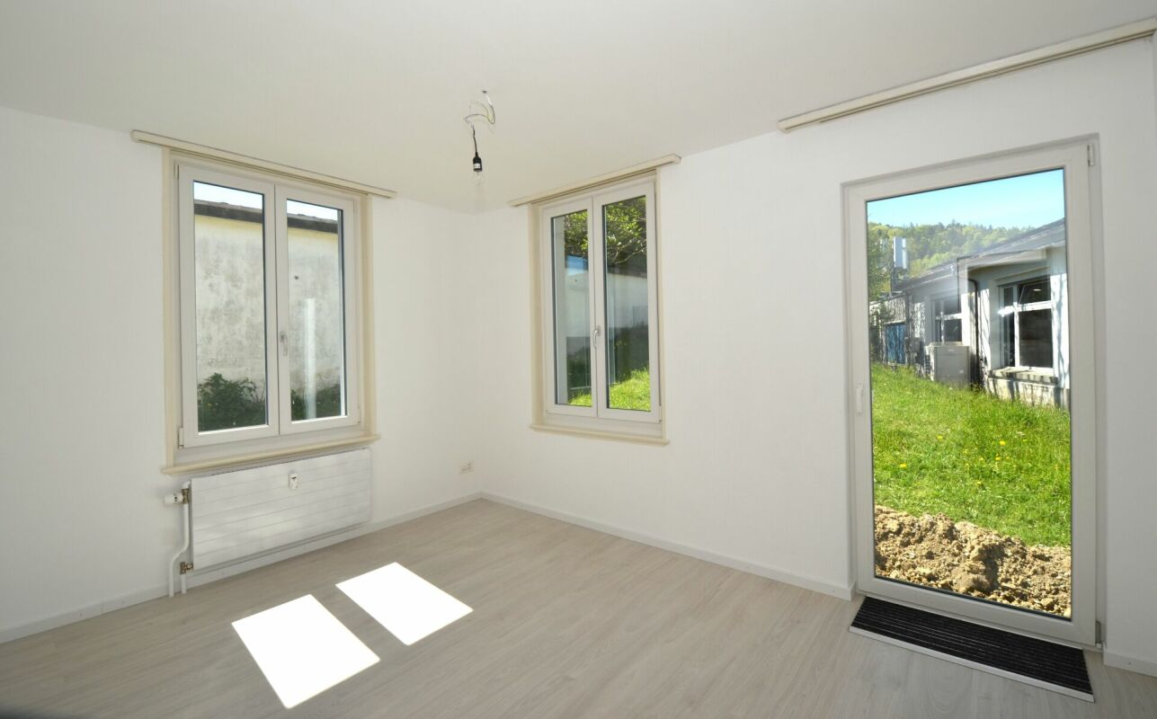 Heller leerer Raum mit drei Fenstern und Gartenzugang