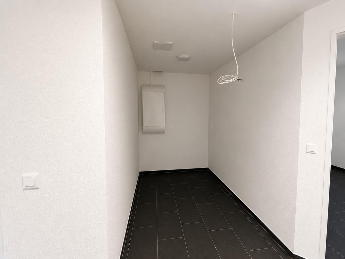 Schmaler, leerer Flur mit dunklen Bodenfliesen und weißen Wänden