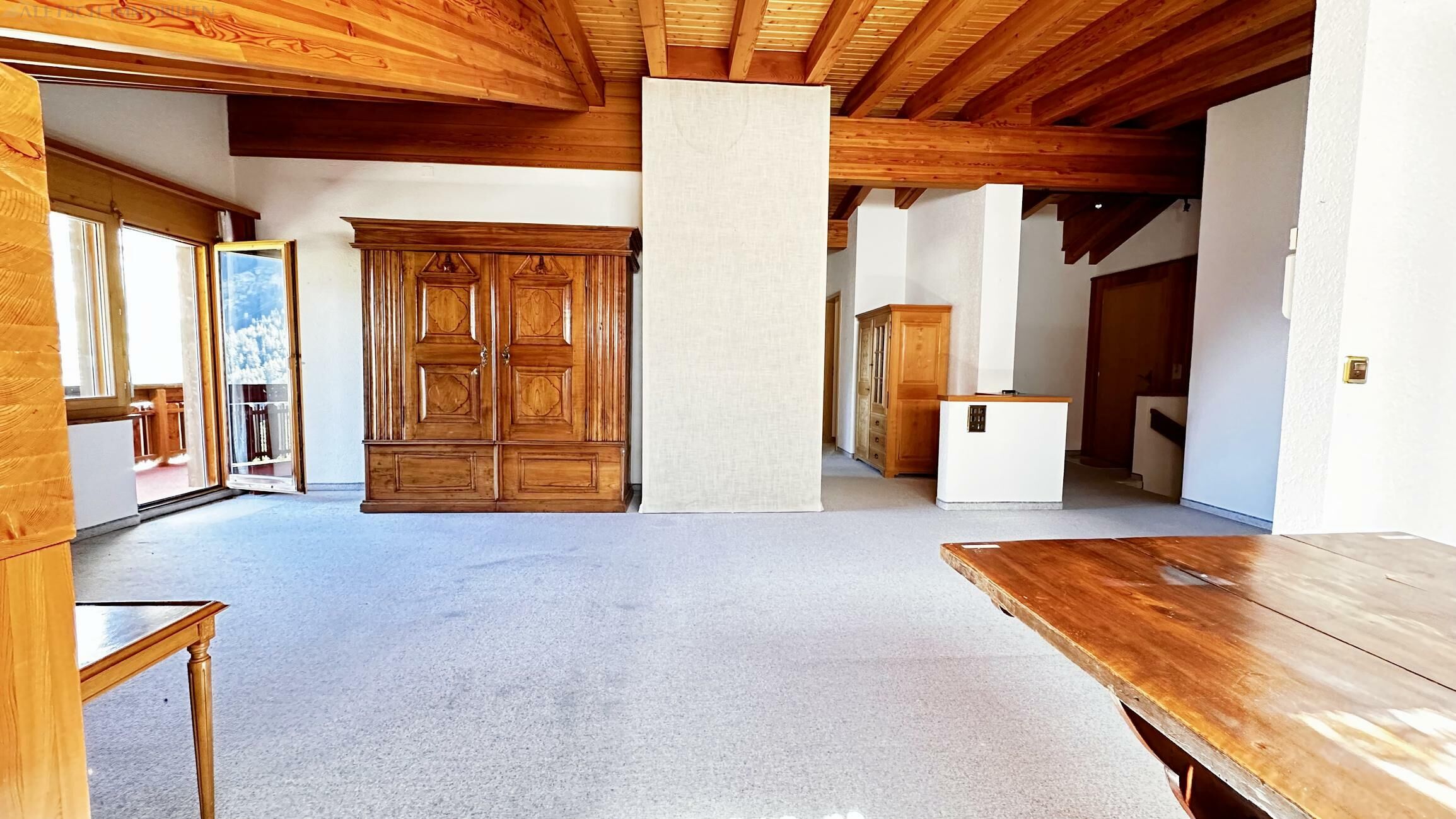 Großer Wohnraum mit Holzdecke und Balkonzugang