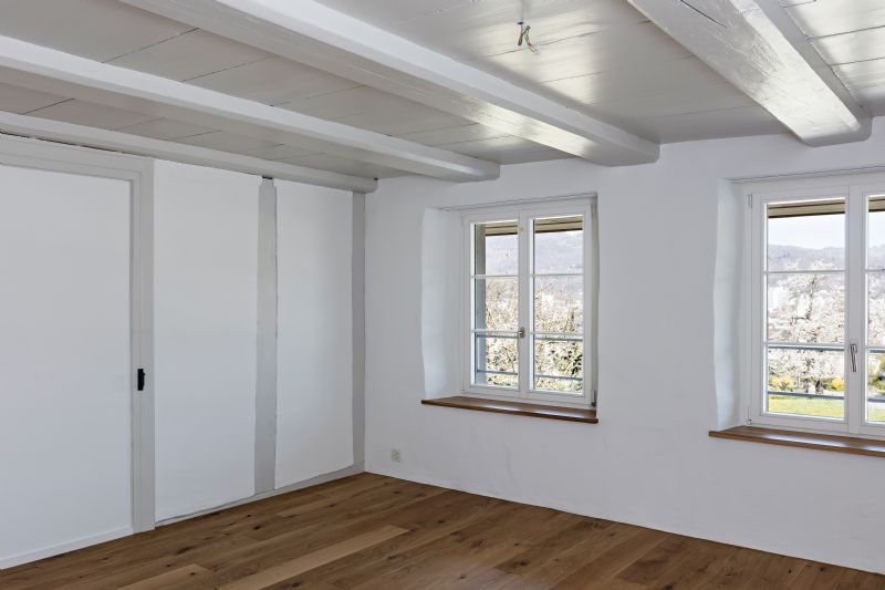 Heller leerer Innenraum mit Holzbalkendecke und zwei Fenstern