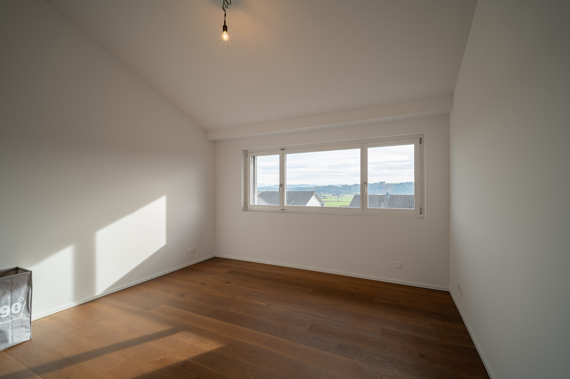 Helles, leeres Zimmer mit großem Fenster und Holzboden