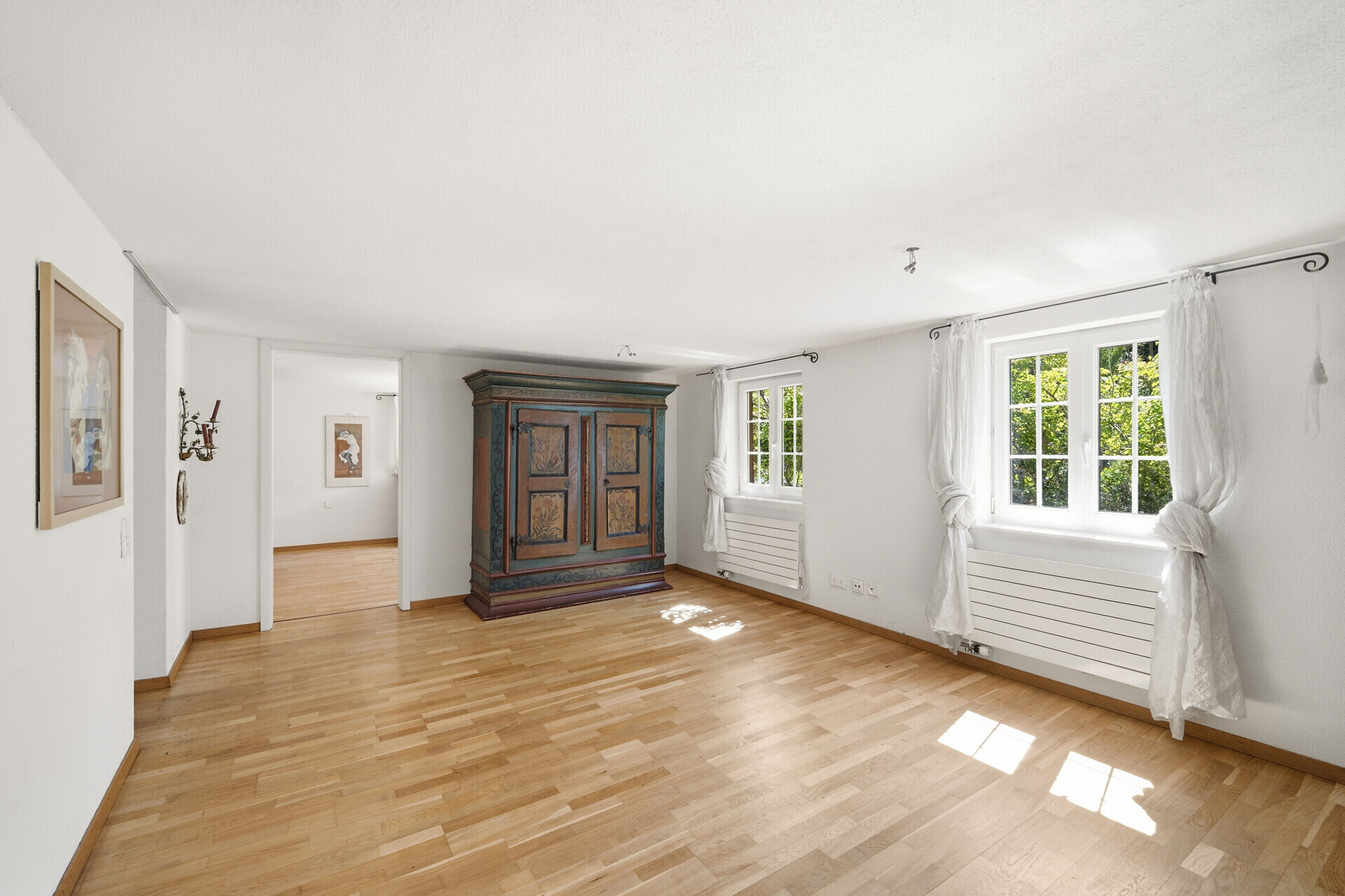 Heller leerer Raum mit Holzparkett und antikem Schrank