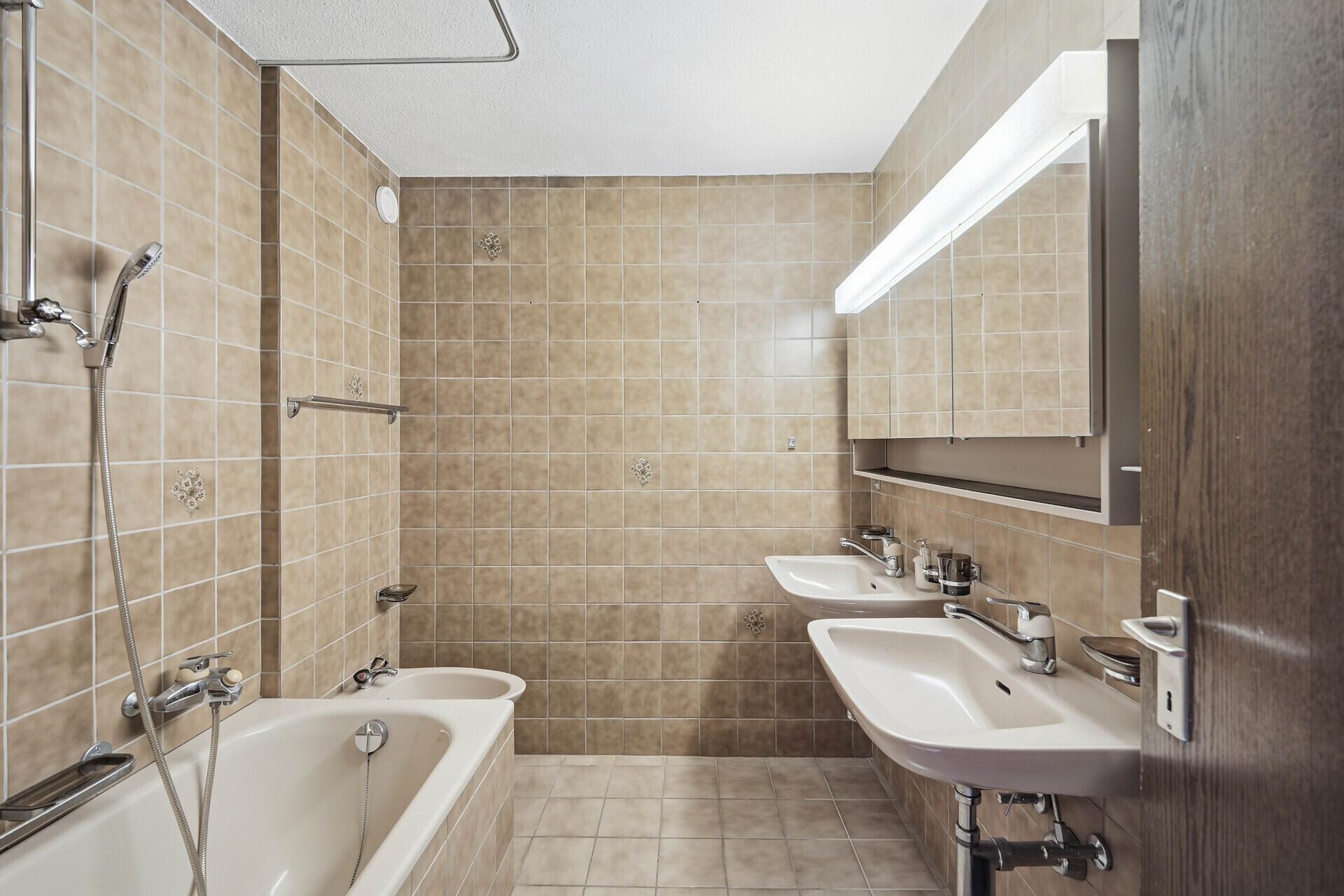 Badezimmer mit Badewanne, Doppelwaschtisch und beigen Fliesen