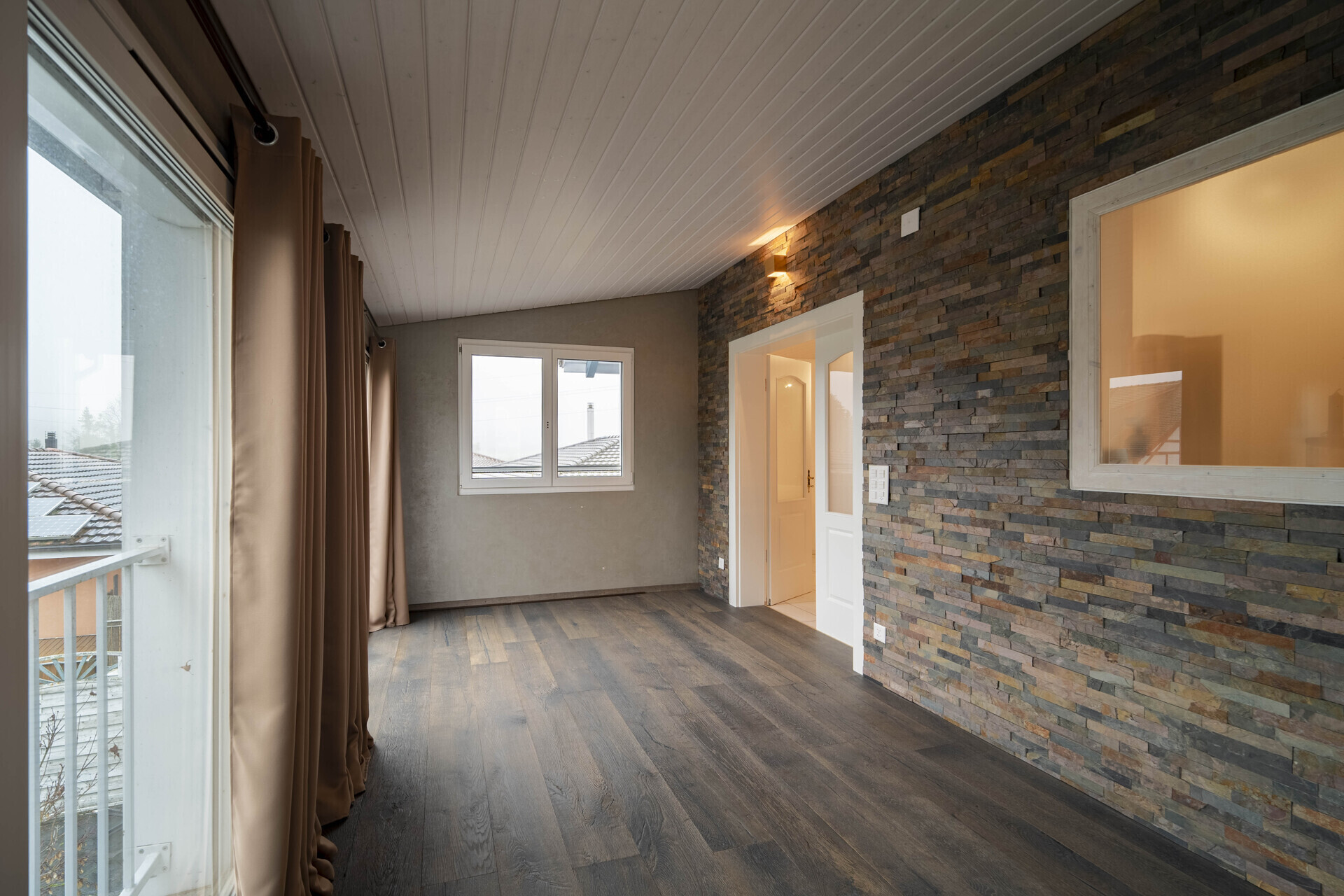 Helles Dachzimmer mit Steinwand und Balkon