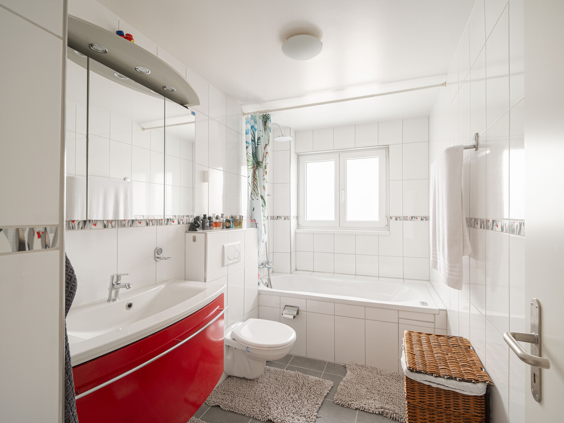 Helles Badezimmer mit Badewanne und rotem Waschtisch