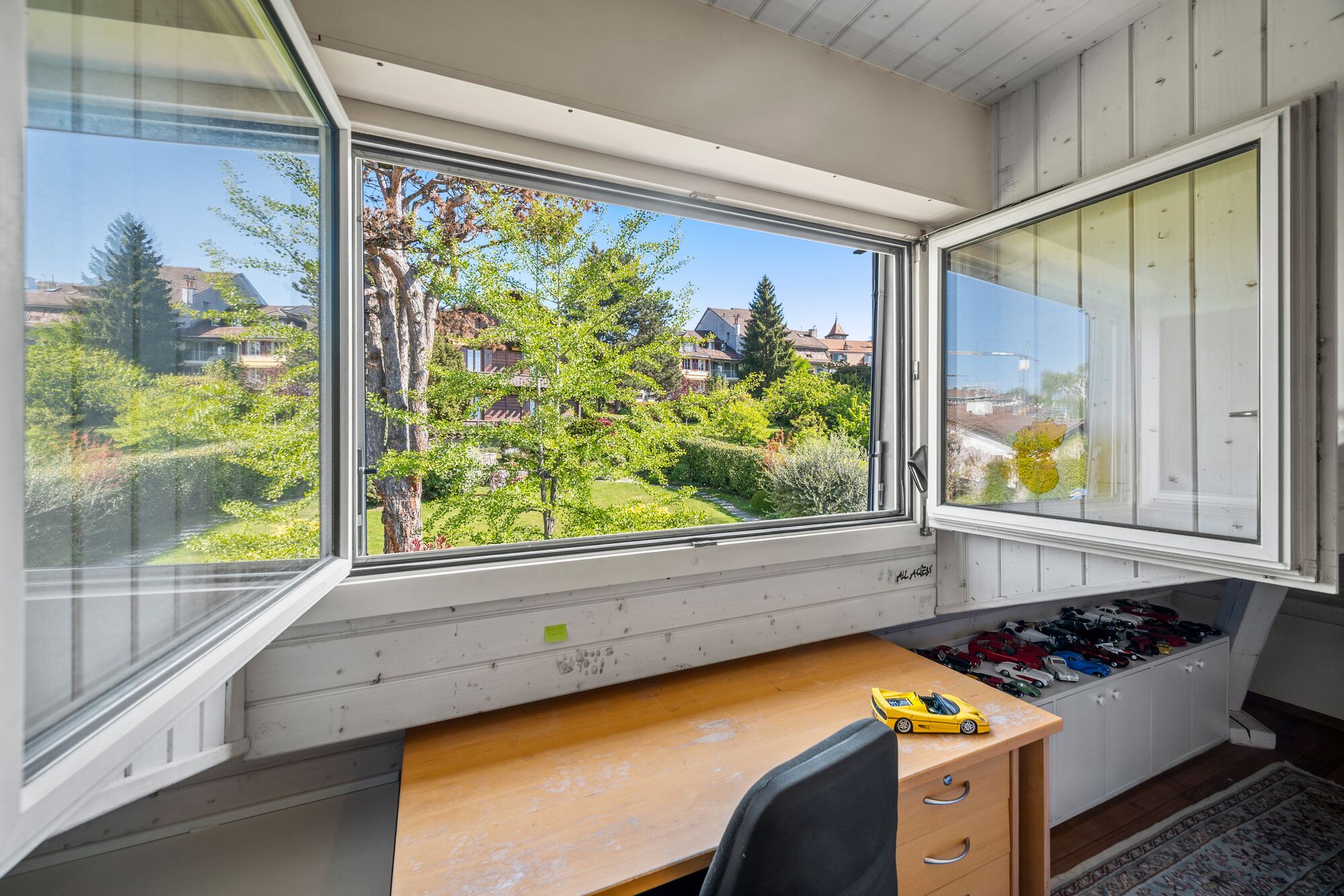 Dachzimmer mit geöffnetem Fenster und Gartenblick
