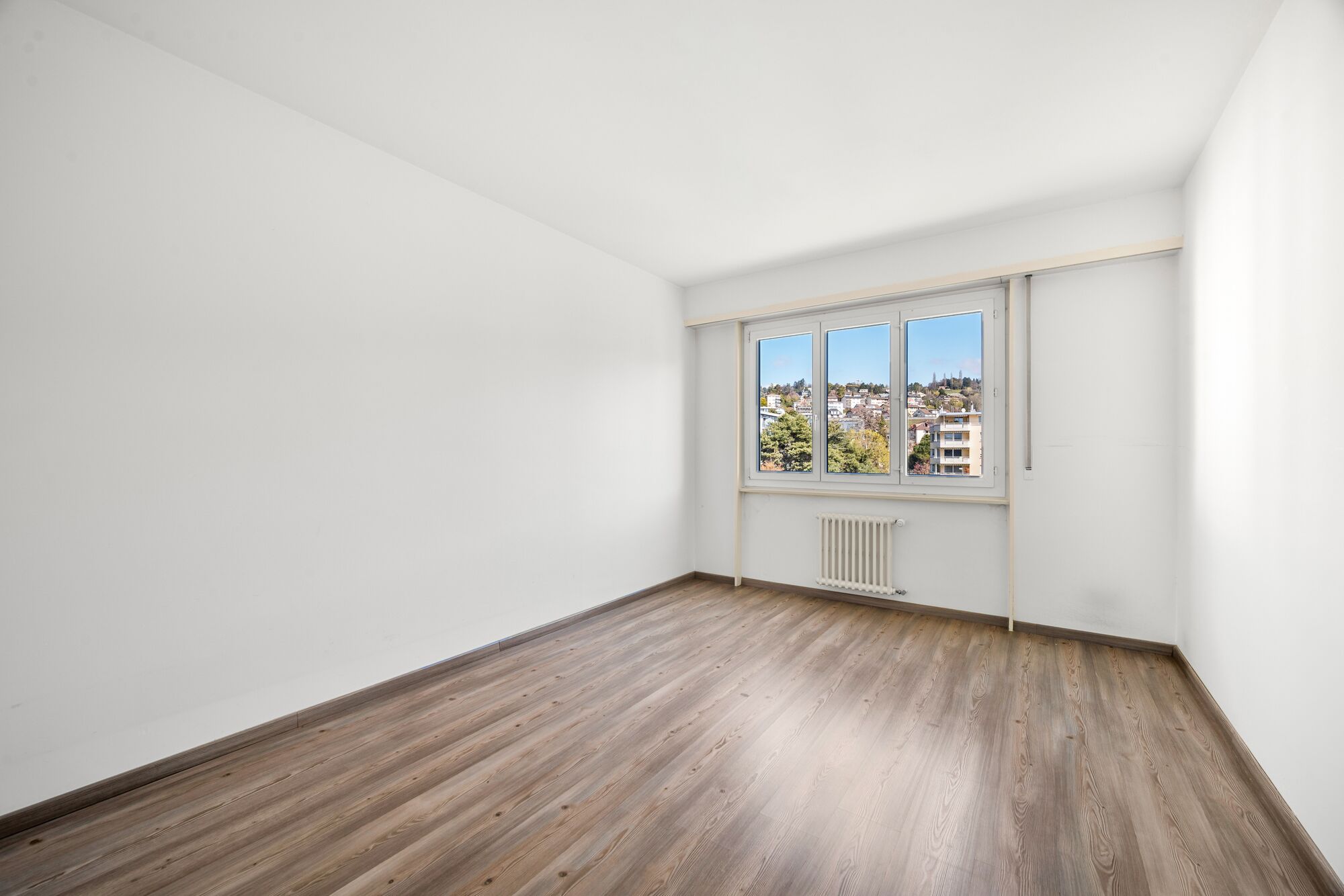 Leerer heller Wohnraum mit Fenster und Holzoptikboden
