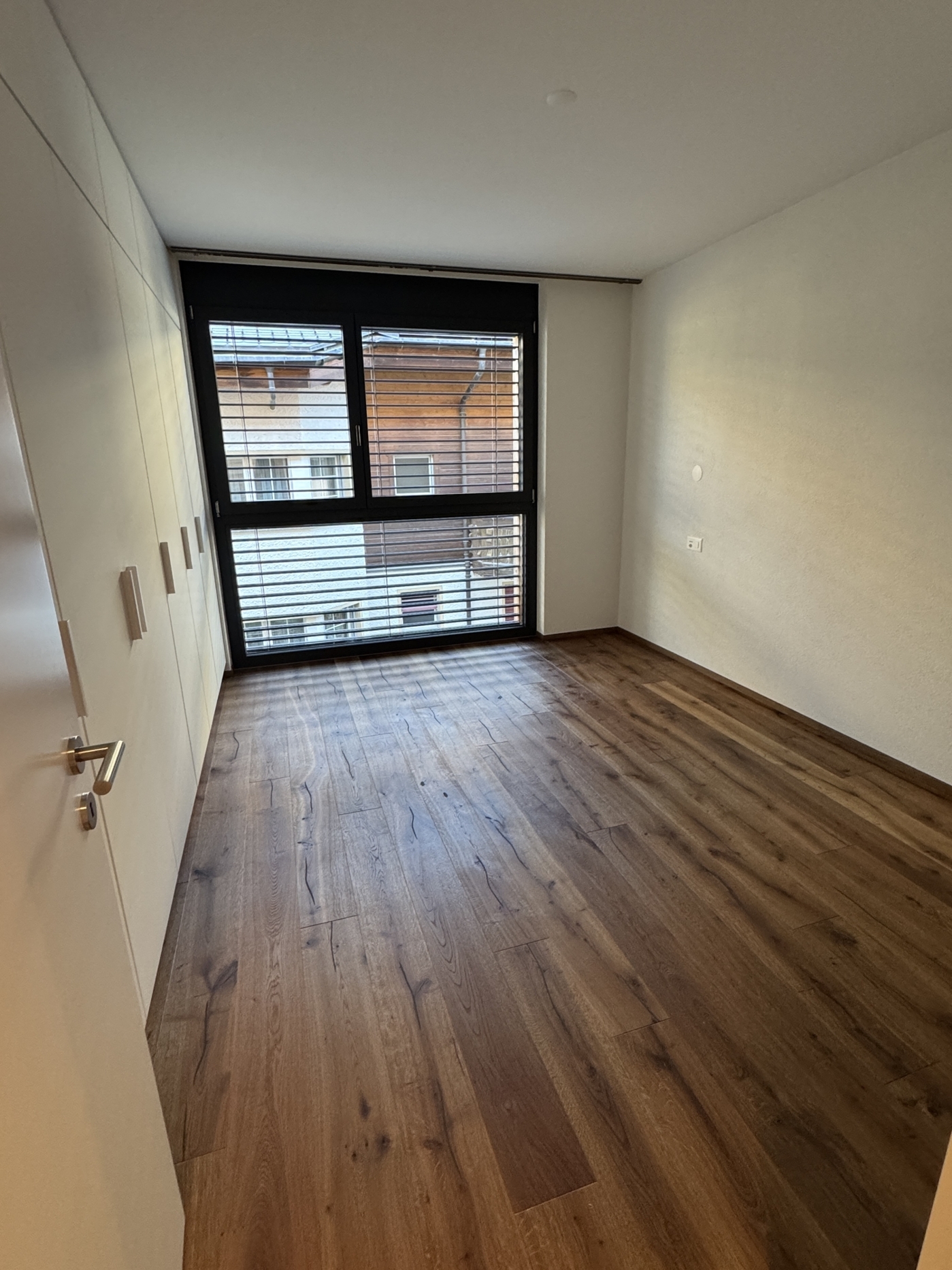 Helles, leerstehendes Zimmer mit großem Fenster und Holzfußboden