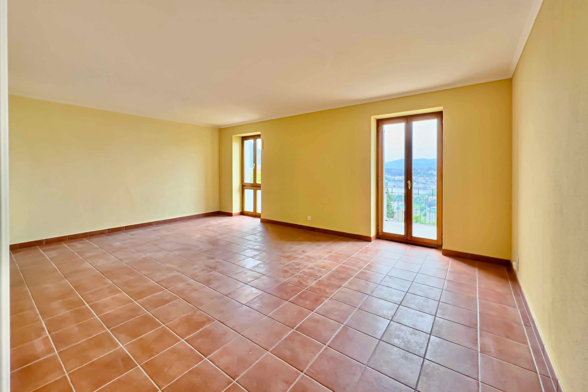 Leerer Wohnraum mit Fliesenboden und Balkonblick