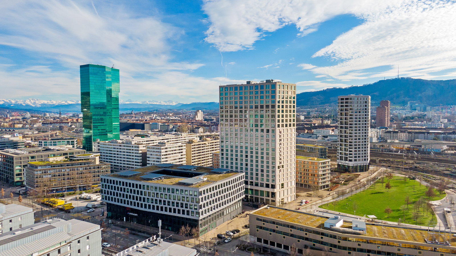 Stadtansicht mit Hochhäusern und Alpenpanorama