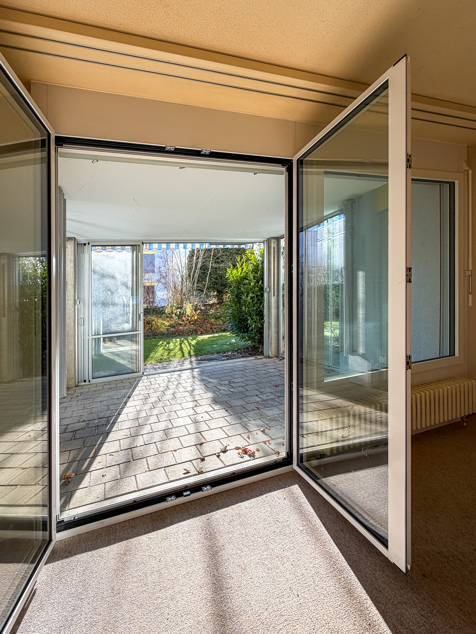 Heller Wintergarten- oder Terrassenraum mit geöffneten Glastüren zum Garten