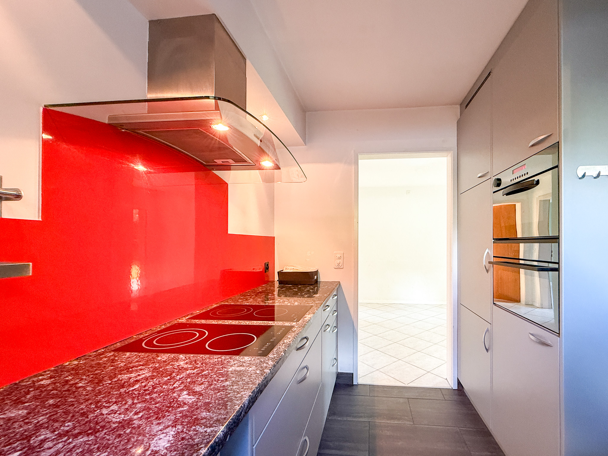 Moderne, schmale Küche mit roter Glasrückwand