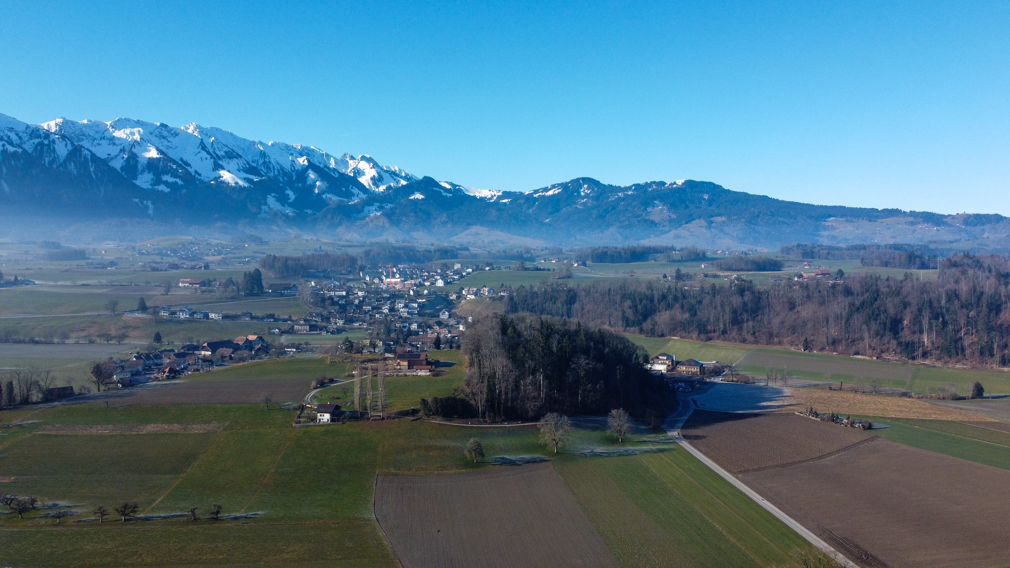 Luftaufnahme eines Alpenvorlands mit Dorf und Bergen