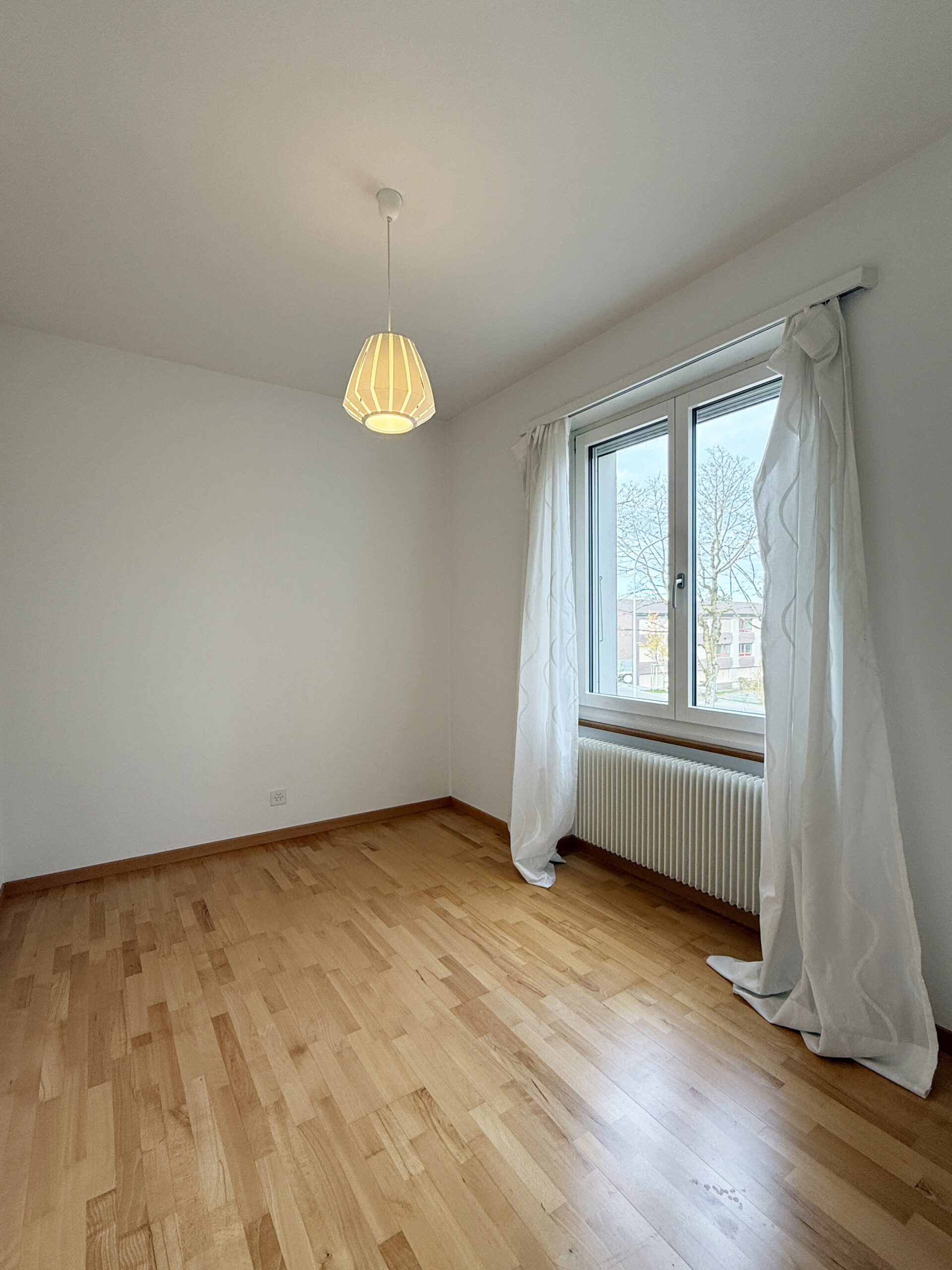 Helles, leeres Zimmer mit Holzboden und Fenster
