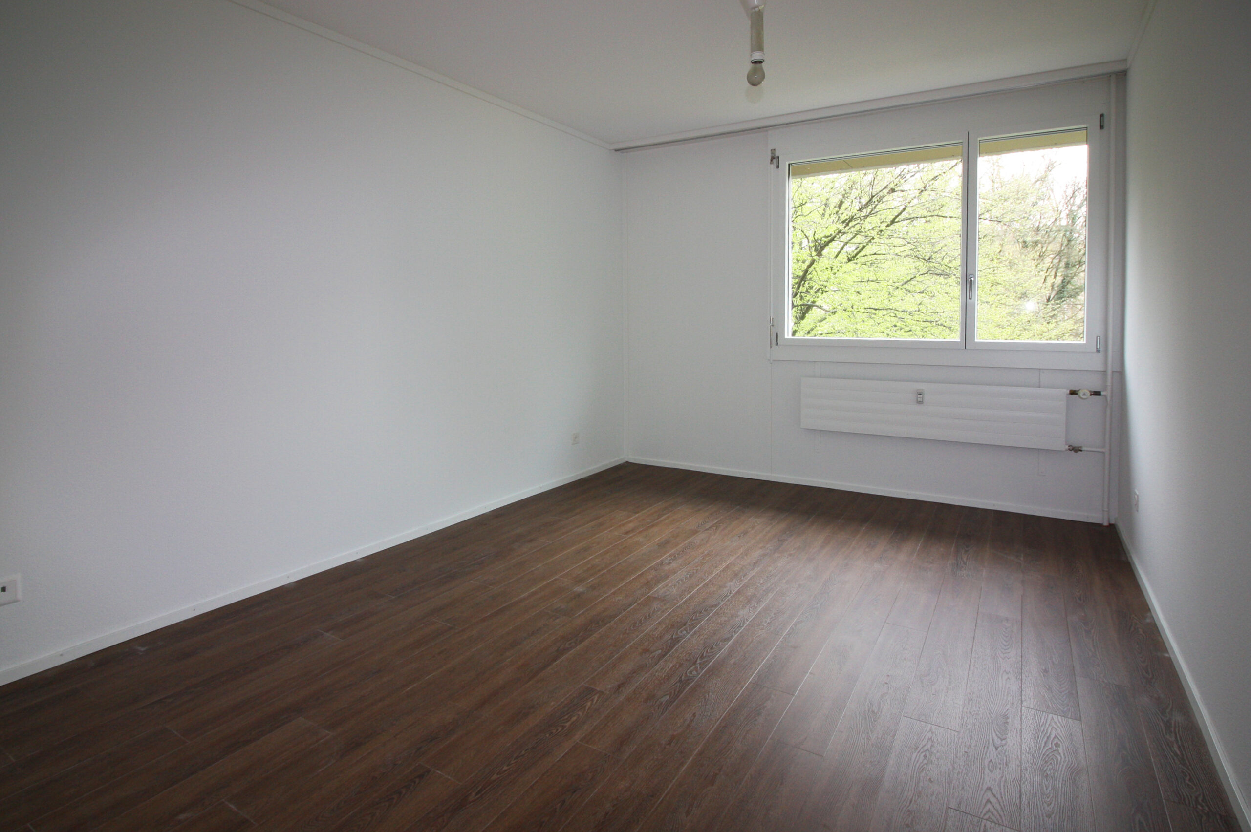 Leerer, heller Raum mit Fenster und dunklem Boden