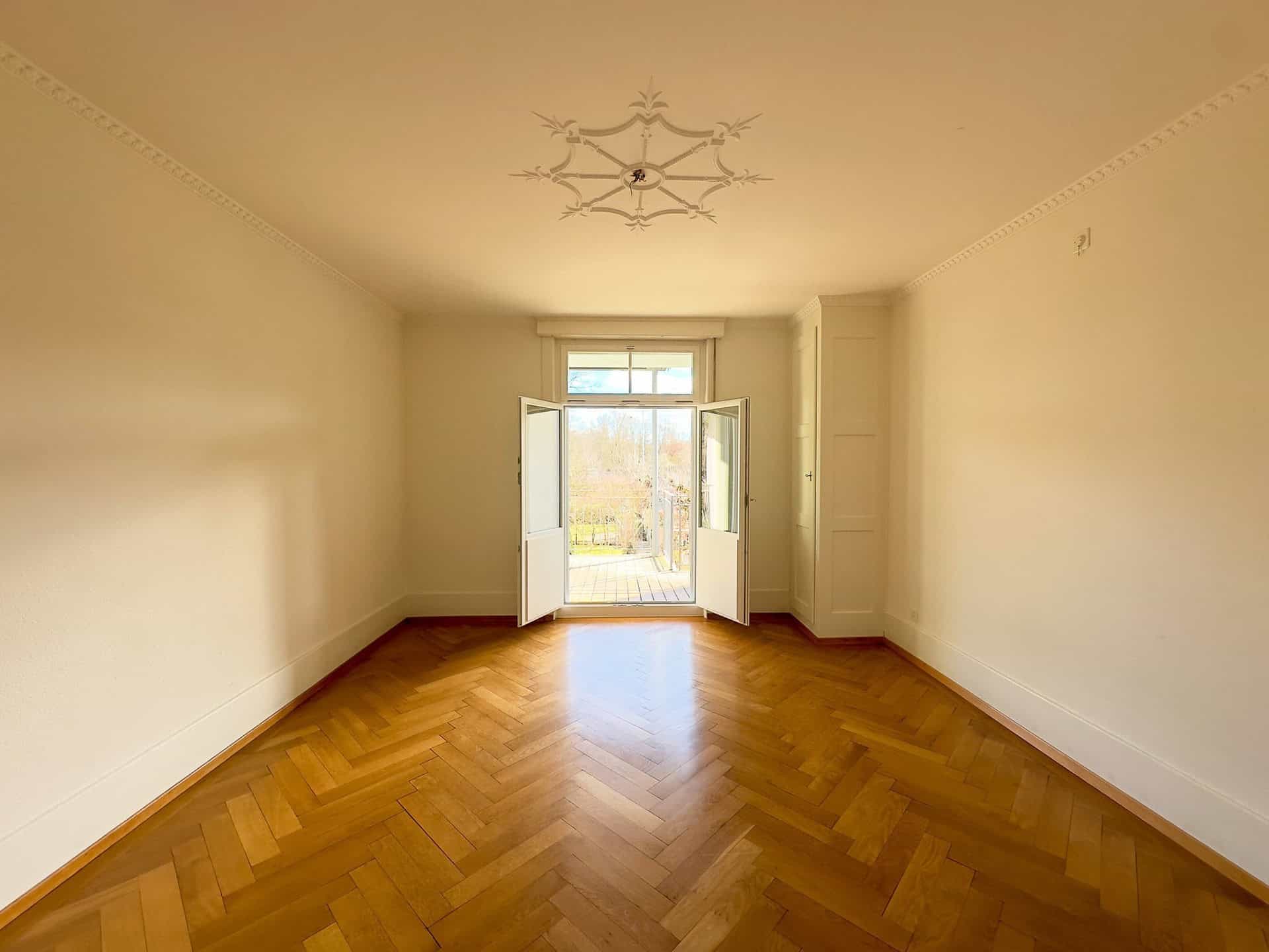 Helles, leeres Zimmer mit Fischgrätparkett und Fenstertür