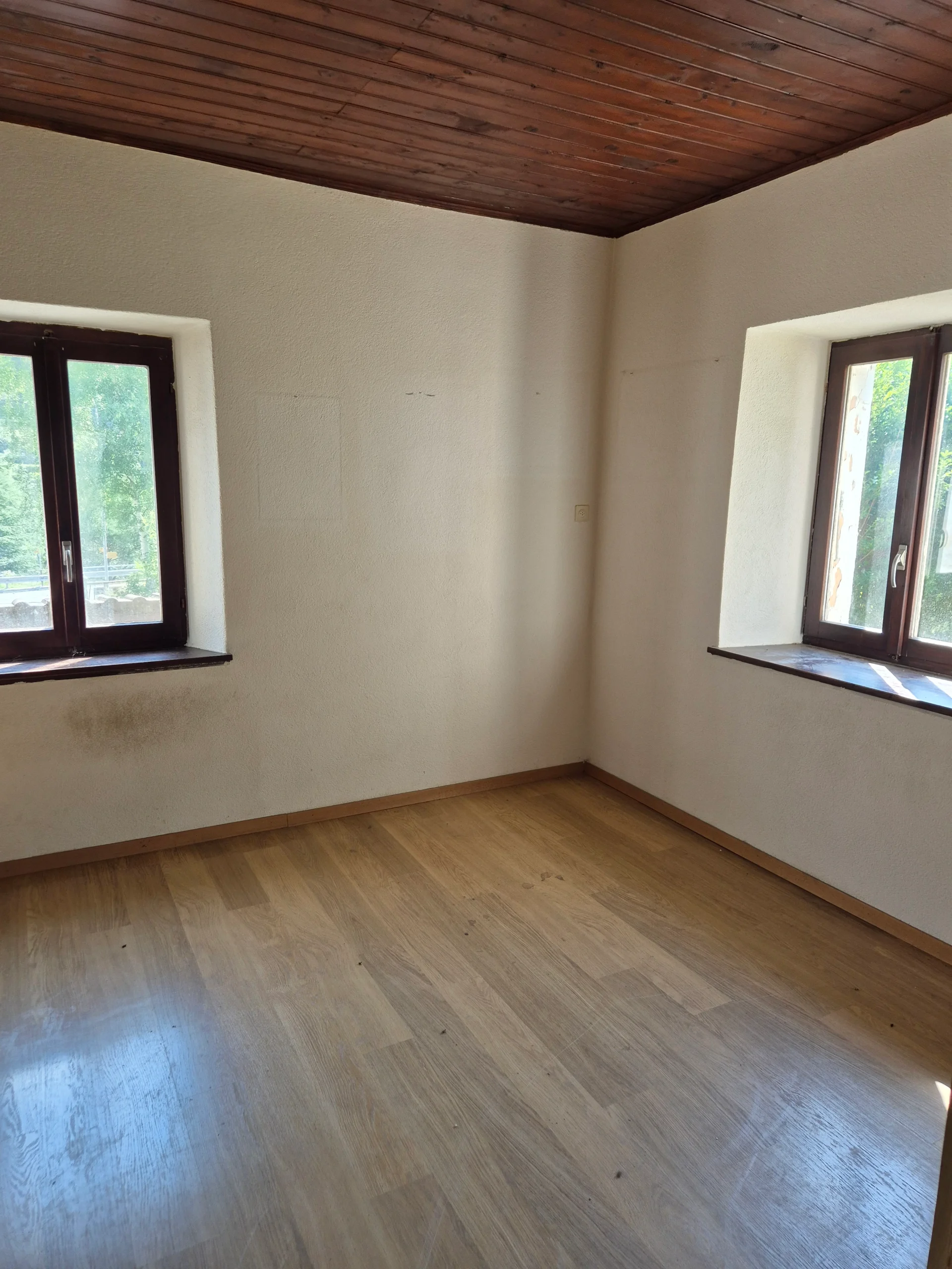 Leerer Raum mit Holzdecke und zwei Fenstern