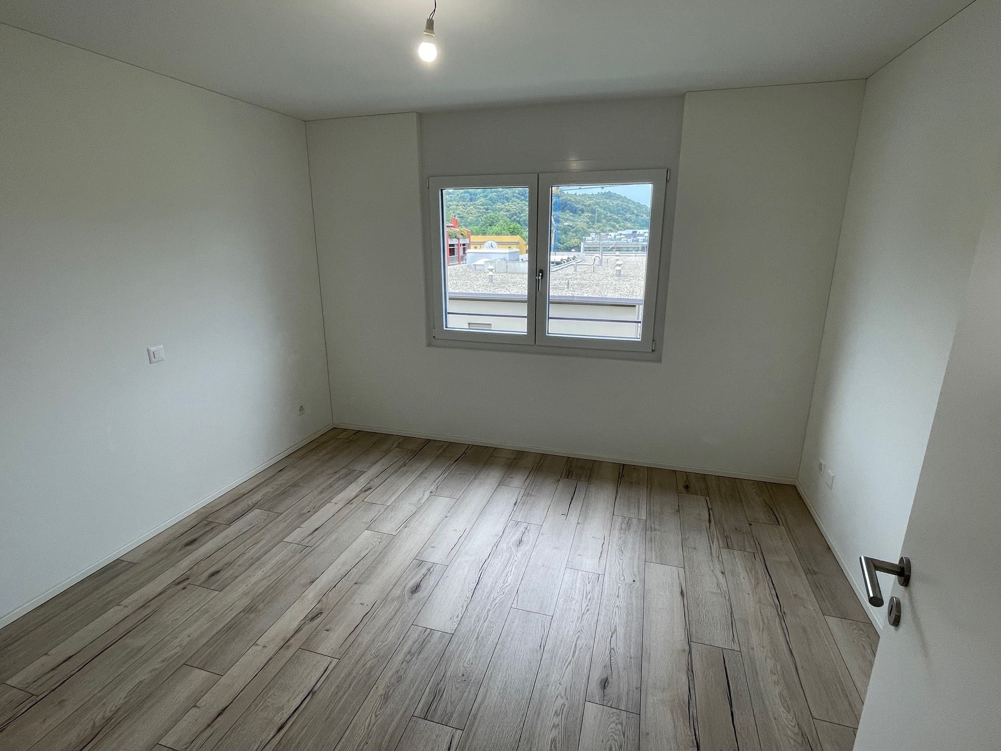 Leeres Zimmer mit Fenster und Holzoptikboden