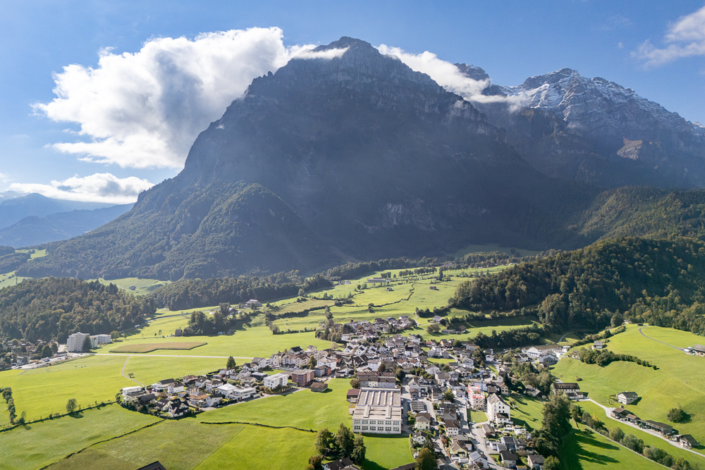 Luftaufnahme eines Alpentals mit Ortschaft und Bergpanorama