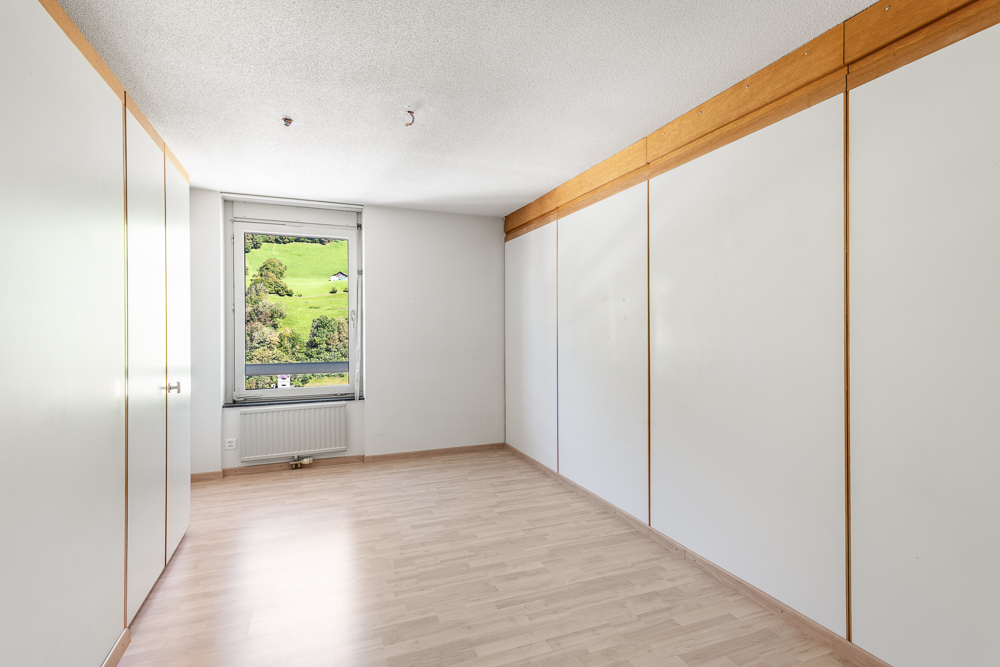 Leerer Raum mit Einbauschränken und Fensterblick ins Grüne
