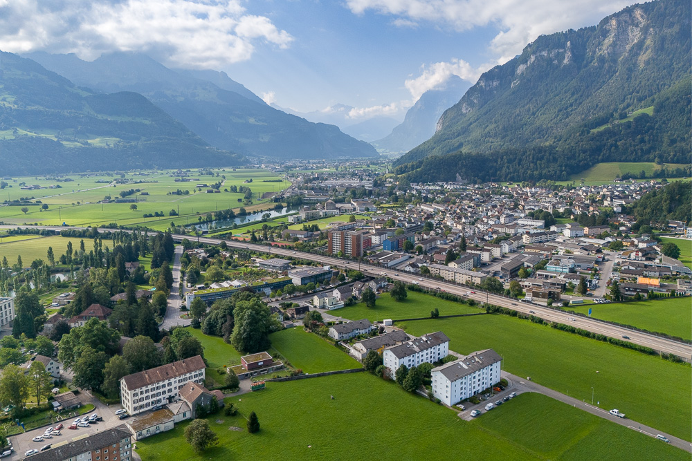 Luftaufnahme eines alpinen Tals mit Stadt und Bergen