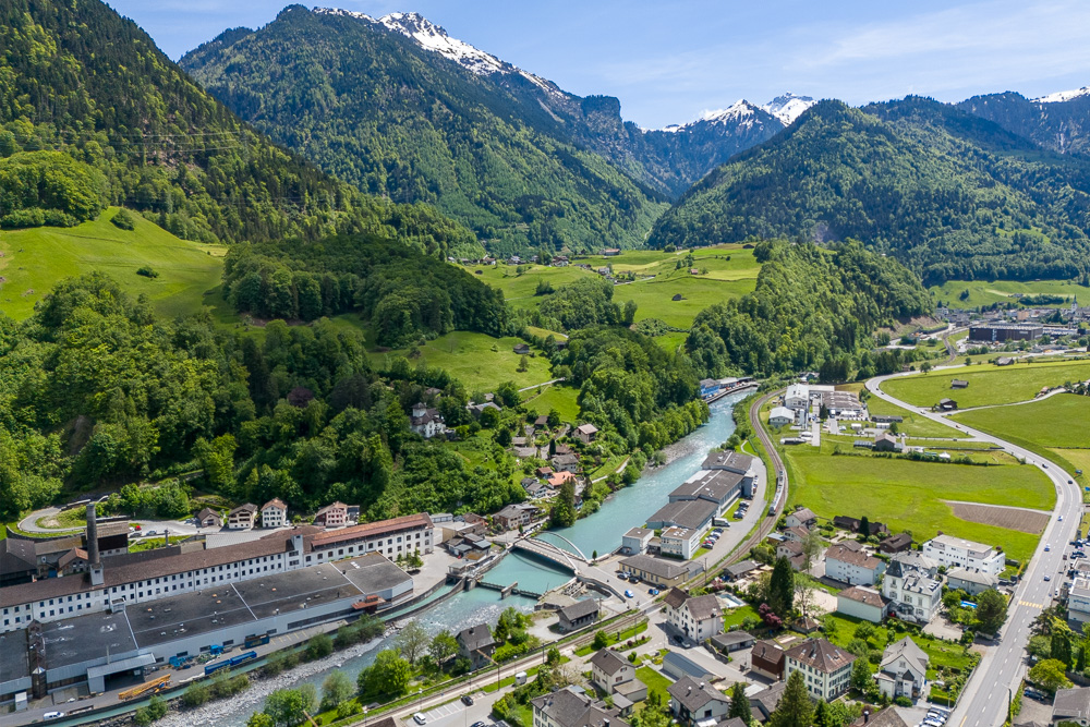 Luftaufnahme eines alpinen Tals mit Fluss und Ortschaft