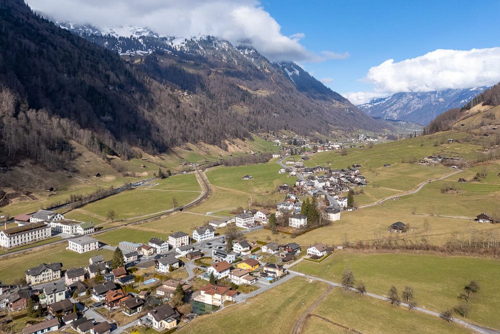 Luftaufnahme eines alpinen Tals mit Dorf und Bergkulisse