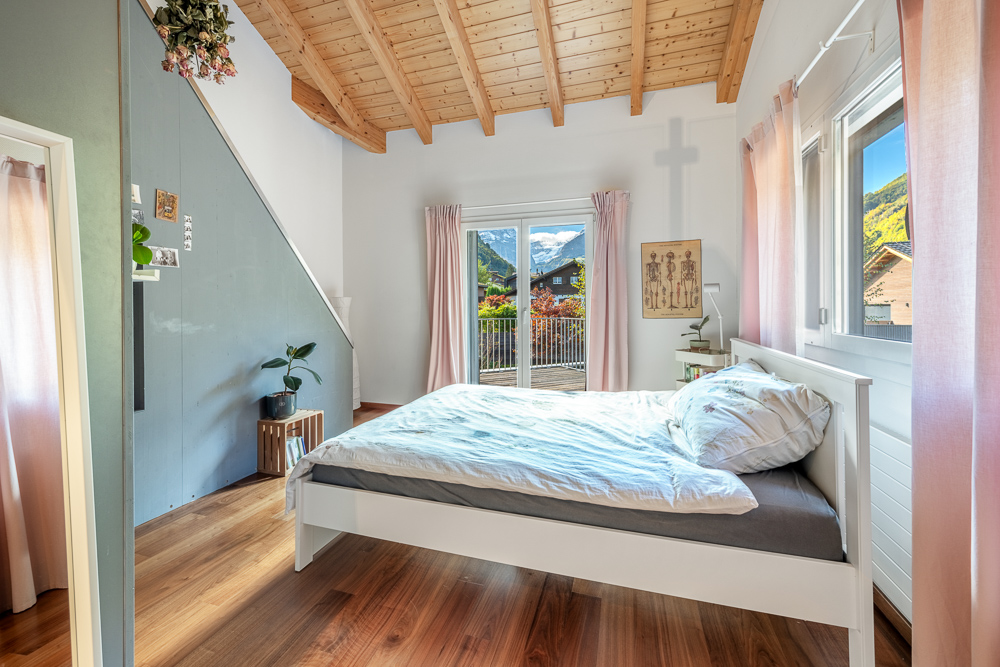 Helles Schlafzimmer mit Holzbalkendecke und Bergblick