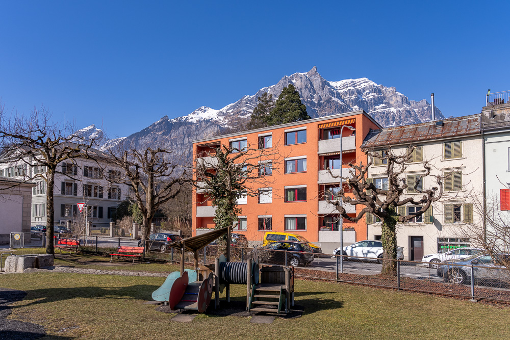 Blick auf Wohnhäuser mit Bergkulisse und Spielplatz