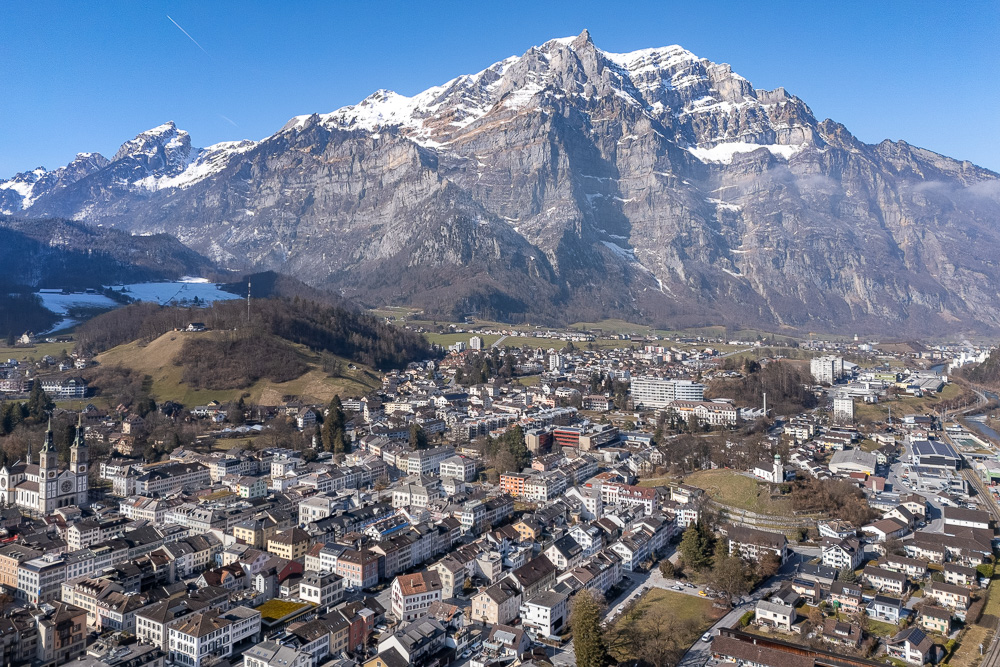 Luftaufnahme einer Stadt vor einer Alpenkulisse