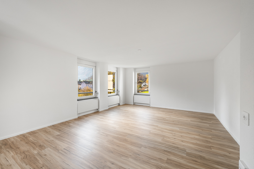 Heller leerer Wohnraum mit Holzoptikboden und drei Fenstern