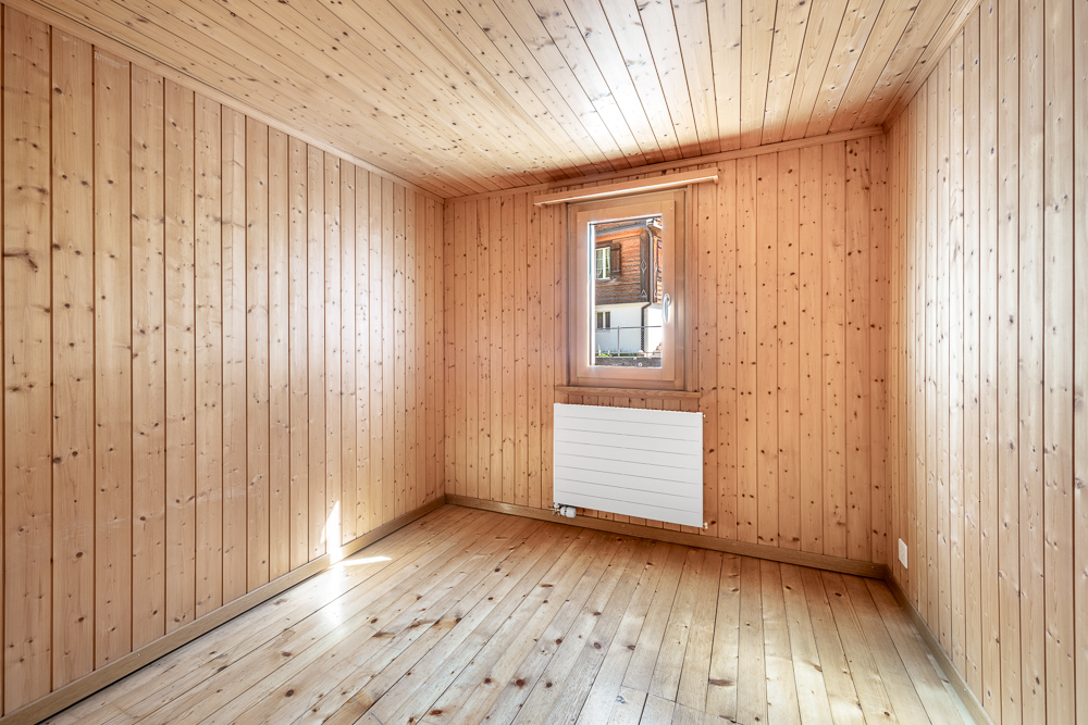 Heller, holzverkleideter Leerraum mit Fenster und Heizkörper
