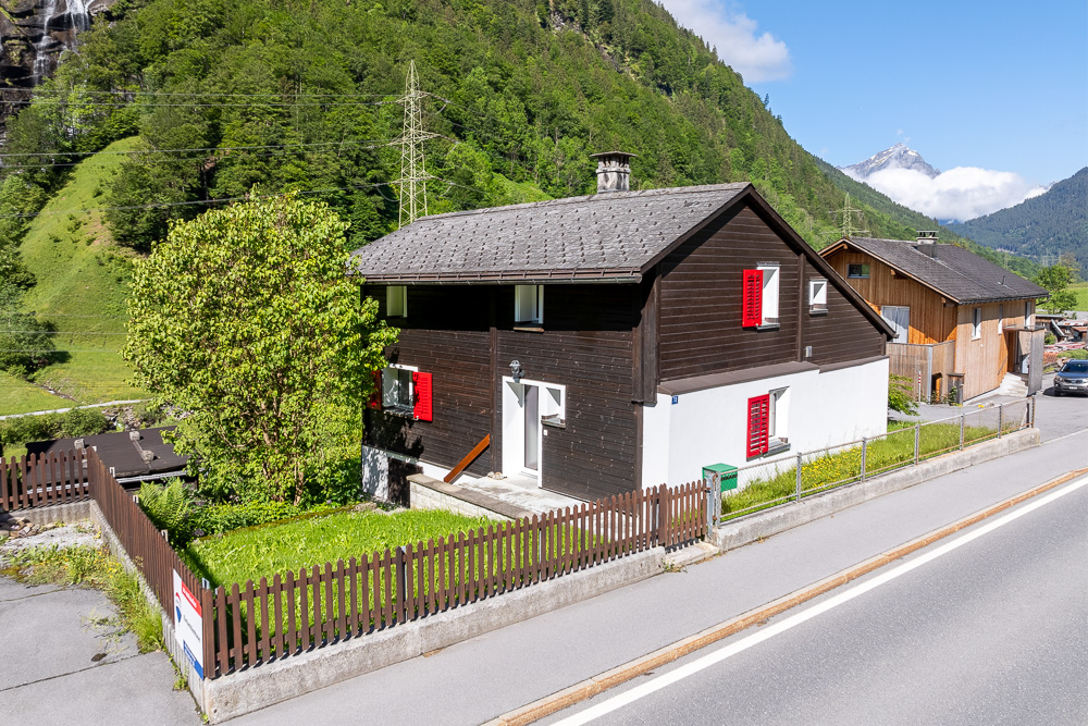 Berghaus mit dunkler Holzfassade und rotem Fensterladen