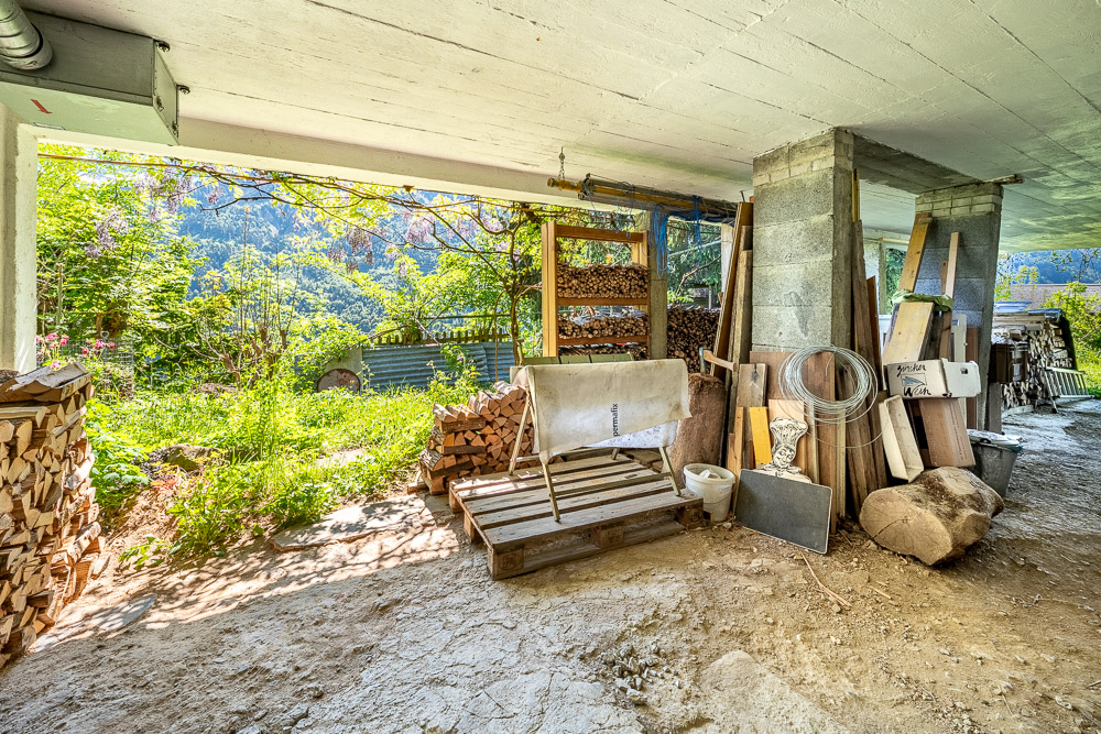 Offener Unterstand mit Holzlager und Gartenblick