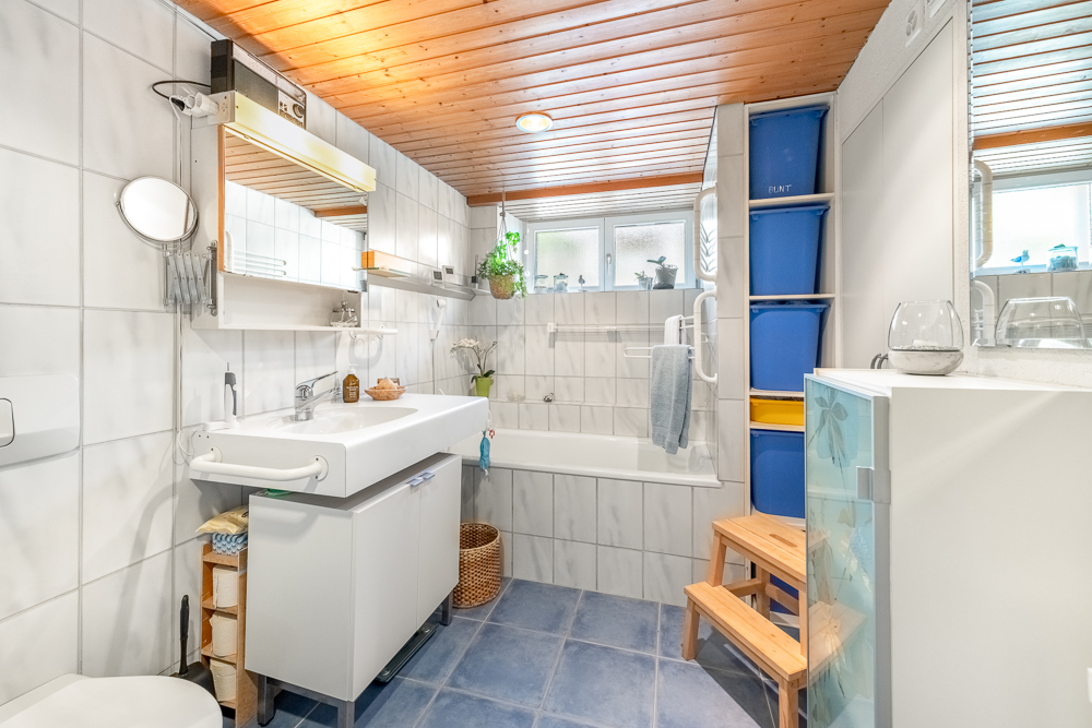 Hell gefliestes Badezimmer mit Badewanne und Holzdecke
