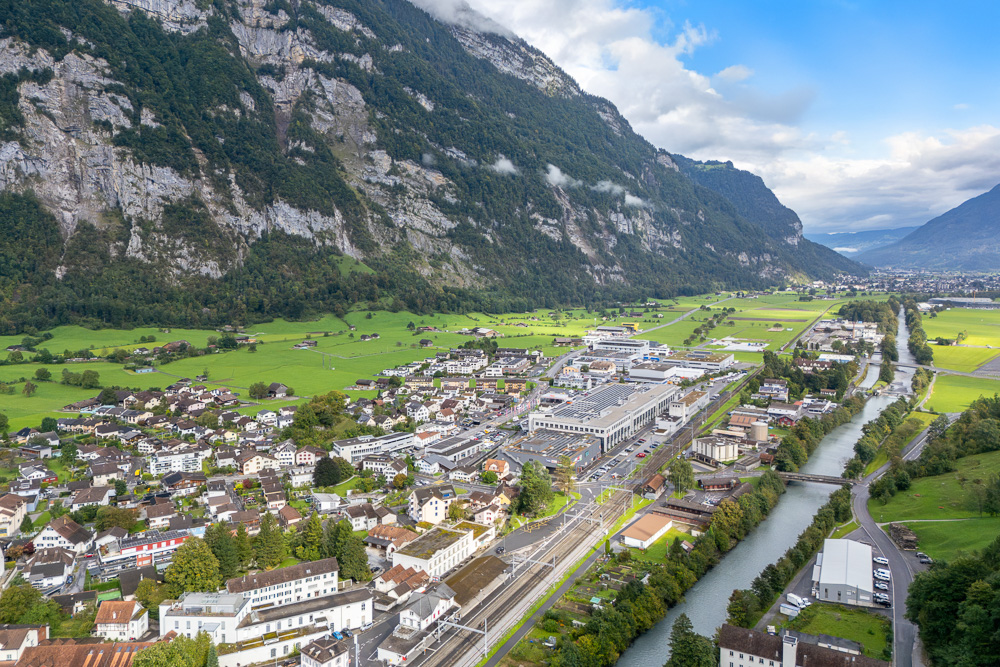 Luftaufnahme eines alpinen Tals mit Stadt, Fluss und Bergen