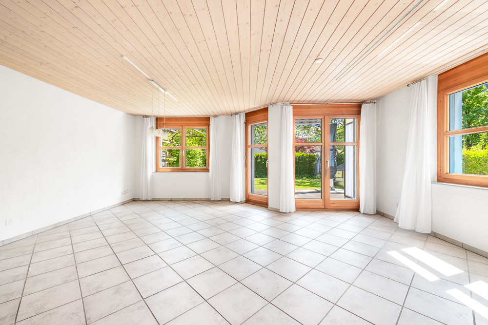 Heller leerer Wohnraum mit großen Holzfenstern und Fliesenboden