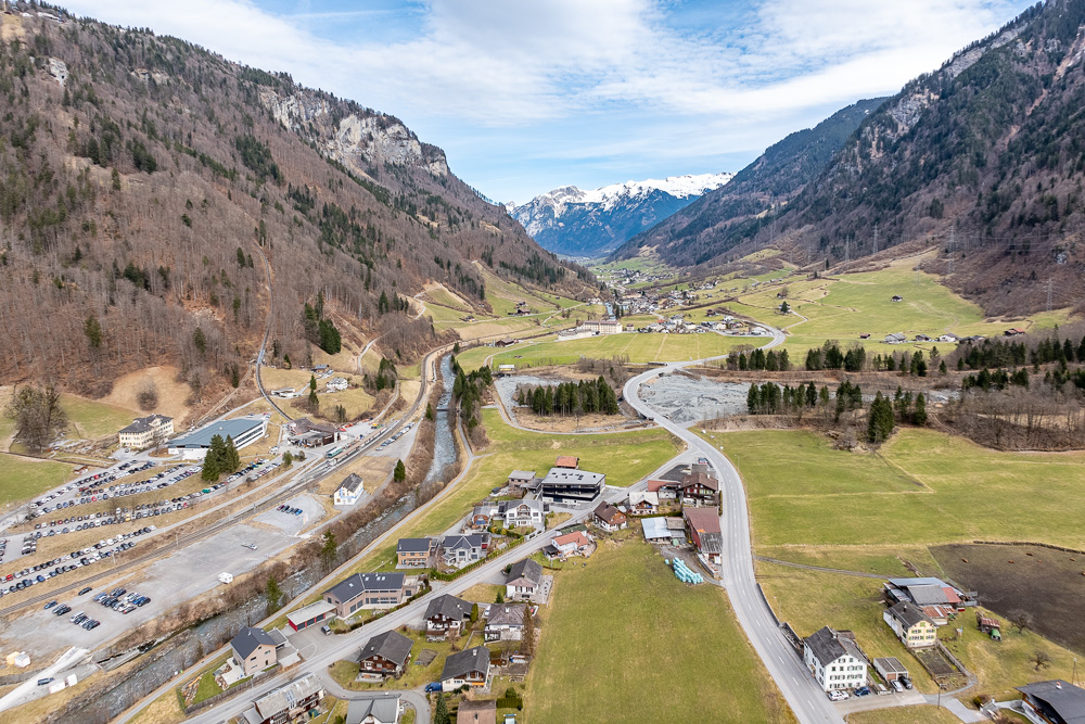 Luftaufnahme eines alpinen Tals mit Straßen, Fluss und verstreuten Gebäuden