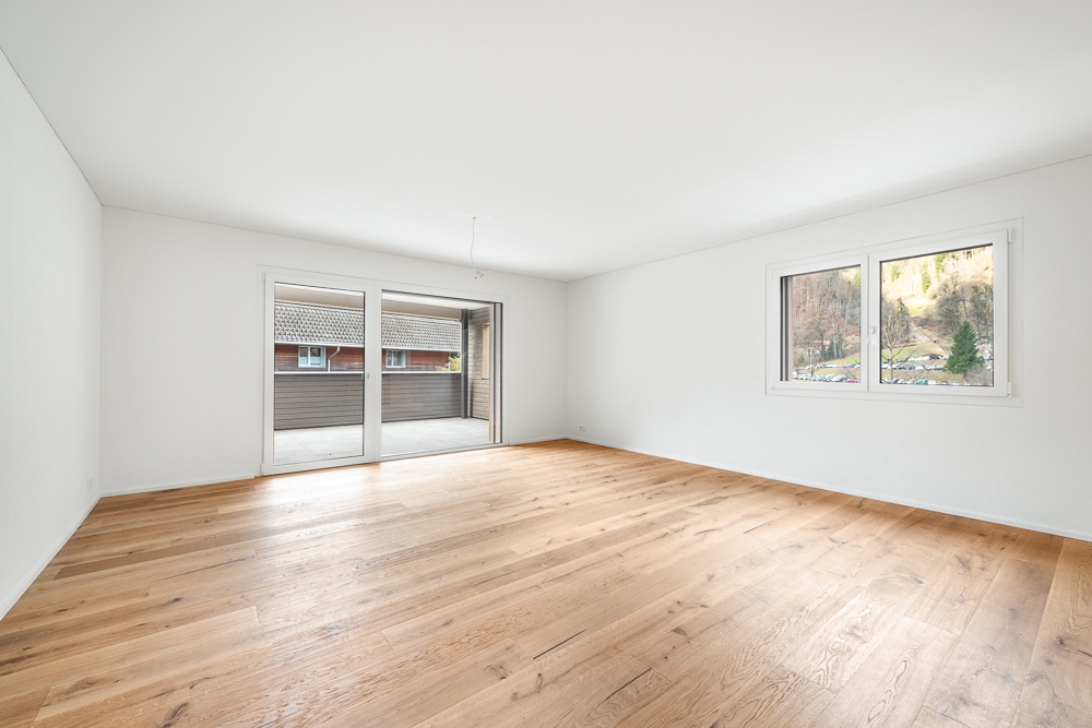 Leerer heller Wohnraum mit Holzboden und Balkonzugang