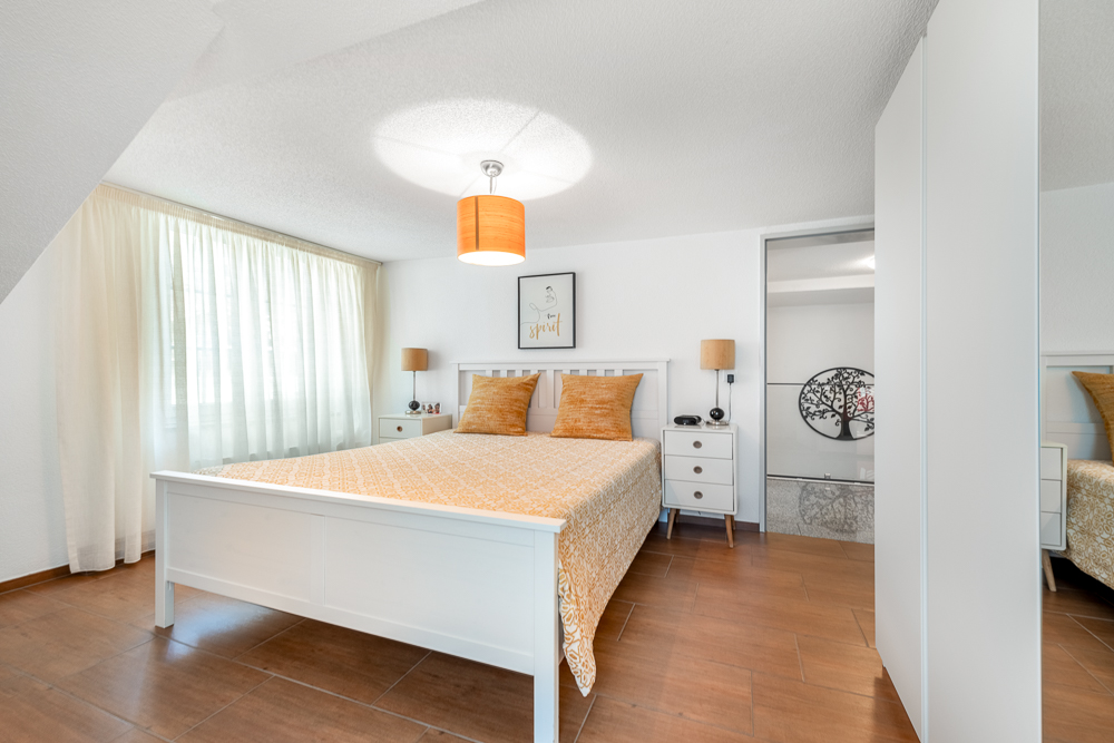 Helles Schlafzimmer mit weißem Bett und Holzoptik-Boden