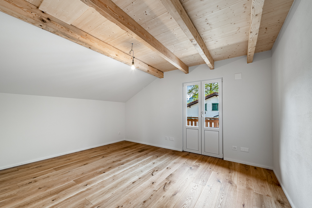 Heller, leerer Dachraum mit sichtbaren Holzbalken und Holzboden