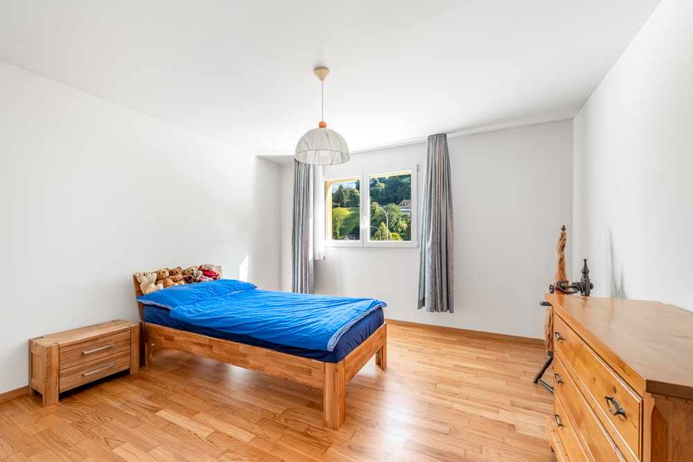 Helles Schlafzimmer mit Holzfußboden und Blick ins Grüne