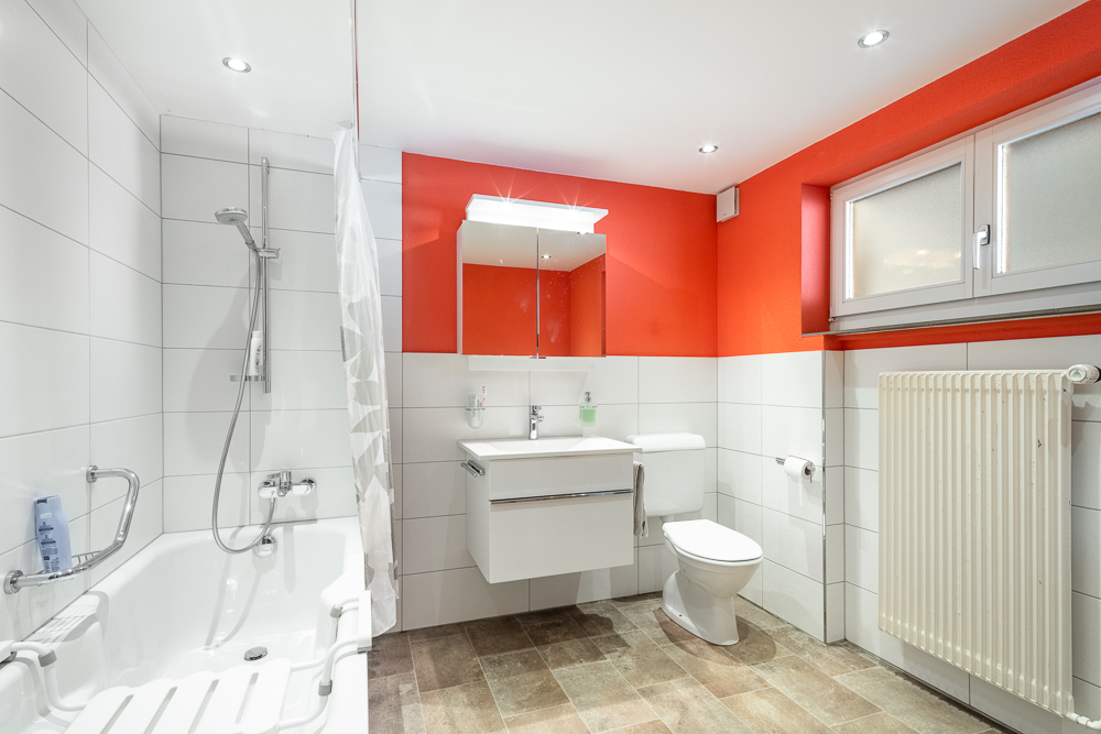 Helles Badezimmer mit Badewanne, Dusche, WC und rot-weißer Gestaltung
