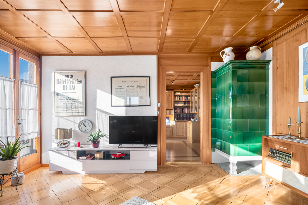 Wohnzimmer mit Holzvertäfelung und grüner Kachelofen-Verkleidung